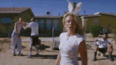 a woman wearing bunny ears and a white shirt is standing in front of a group of people .