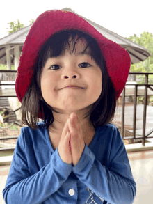 a little girl wearing a red hat and a blue shirt prays