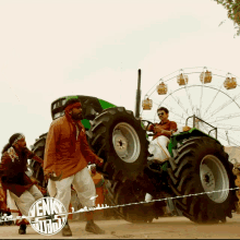 a group of men are dancing in front of a ferris wheel and a sign that says ' vekky ' on it