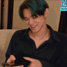 a man with blue hair is smiling while holding a cell phone