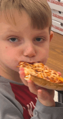 a young boy is eating a slice of pizza in front of a stack of pizza boxes