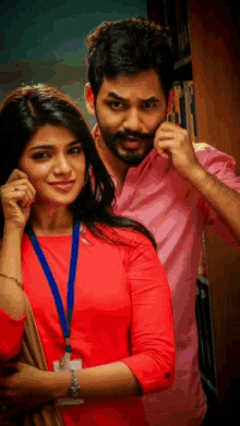 a man with a beard and a woman in a red dress are standing next to each other in a library .