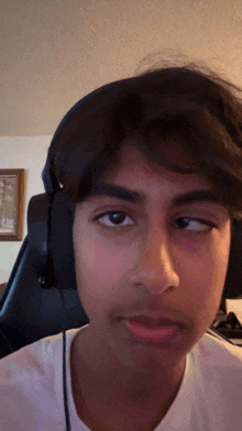 a young man wearing headphones and a white shirt looks at the camera