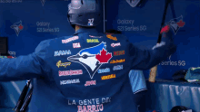 the back of a blue jays player 's jacket says la gente del barrio on the bottom