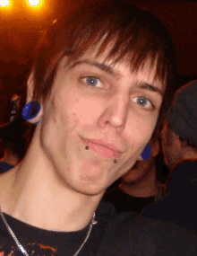 a young man with blue ear plugs and a piercing on his lip