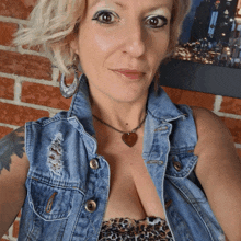 a woman wearing a leopard print top and a denim vest stands in front of a brick wall