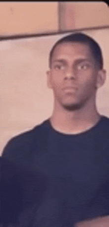 a young man in a black shirt is standing in front of a wall .