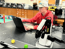 a man sitting at a desk with a laptop and a robotic arm in front of him