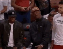 a group of men are standing in a stadium watching a basketball game . one of the men is wearing a hat .