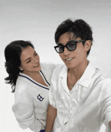 a man wearing sunglasses stands next to a woman wearing a white sweater with the letter b on it