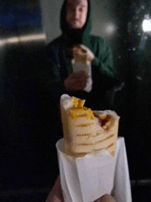 a man in a green hoodie is holding a sandwich in front of him