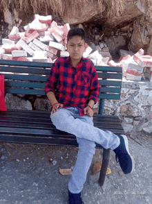 a young boy sits on a bench with a pile of bricks behind him