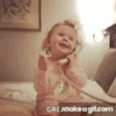a little girl is sitting on a bed talking on a phone .