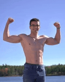 a shirtless man is flexing his muscles while standing next to a lake .