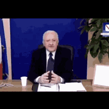 a man in a suit and tie is sitting at a desk with a cup in front of him .