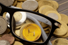 a pair of glasses sits on top of a pile of coins with a gold coin with the letter h on it