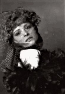 a black and white photo of a woman with curly hair wearing a hat and feathers .