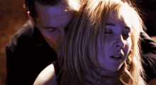 a man holds a woman 's neck in a dark room with her eyes closed