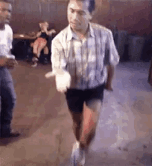 a man in shorts and a plaid shirt is dancing in a room .