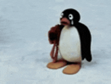 a stuffed penguin is standing in the snow holding a stuffed animal in its mouth .