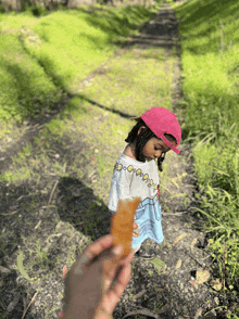 a little girl in a pink hat holds a piece of food