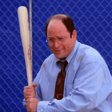 a man is holding a baseball bat in front of a chain link fence .