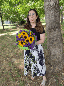 a woman holds a bouquet of sunflowers and purple carnations