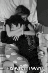 a man and a woman are hugging each other on a bed in a black and white photo .