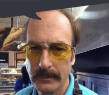 a bald man with a mustache and yellow sunglasses is standing in a kitchen .