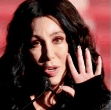 a close up of a woman talking into a microphone while holding her hand to her face .