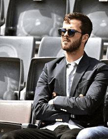 a man wearing sunglasses sits in a stadium