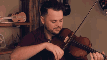 a man playing a violin in front of a shelf with a pink guitar that says ' elvis ' on it