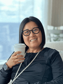 a woman wearing glasses holds a cup of coffee that says ' o ' on it