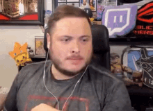 a man with a beard wearing headphones is sitting in a chair in front of a shelf with stuffed animals .