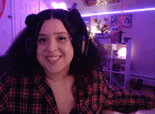 a woman wearing a plaid shirt and headphones smiles in front of a sign that says cafe margarita