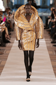 a model walks down the runway wearing a gold dress