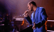 a man in a blue suit is singing into a microphone on a stage in front of a keyboard .