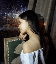 a woman sitting in front of a window with rain drops on the glass