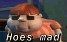 a cartoon character wearing sunglasses and the words `` hoes mad '' is sitting in a chair .