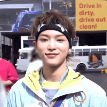 a young man wearing a headband stands in front of a yellow sign that says drive in dirty drive out clean