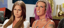two women with pink hair are sitting next to each other on a couch making funny faces .