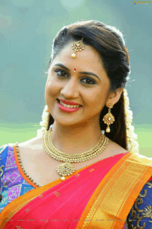 a woman wearing a pink and orange saree and gold jewelry smiles for the camera