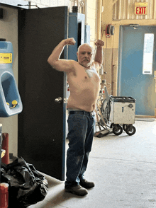 a shirtless man flexes his muscles in front of a red exit sign