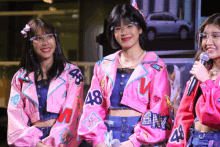 three girls wearing pink jackets with the number 48 on them stand next to each other