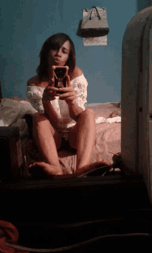 a woman sits on a bed taking a picture of herself in a mirror