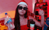 a woman in a santa hat and sunglasses holds a bottle of water