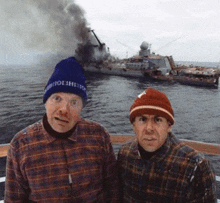 two men are sitting on a boat with a ship in the background .