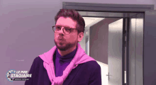 a man wearing glasses and a pink sweater is standing in front of a door that says le pire stagiaire version longue