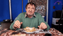 a man in a green sweater is sitting at a table with a plate of food and a sign that says videoinfo