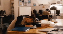 a woman rests her head on a desk with a blue folder on it that says ' a ' on it